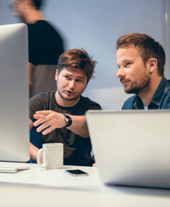 Two guys with coffee and phone looking at a monitor