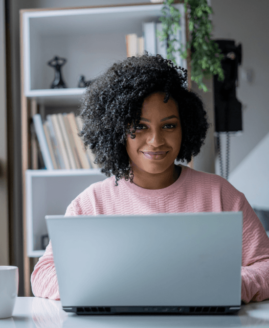 Smiling lady with pink sweater behind laptop